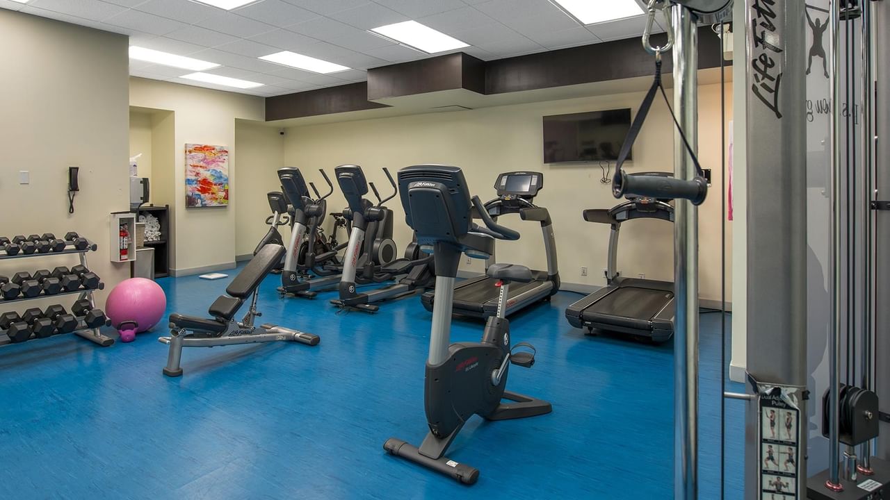 Modern fitness center with cardio machines, free weights, and blue flooring at Coast Calgary University Area Hotel by APA