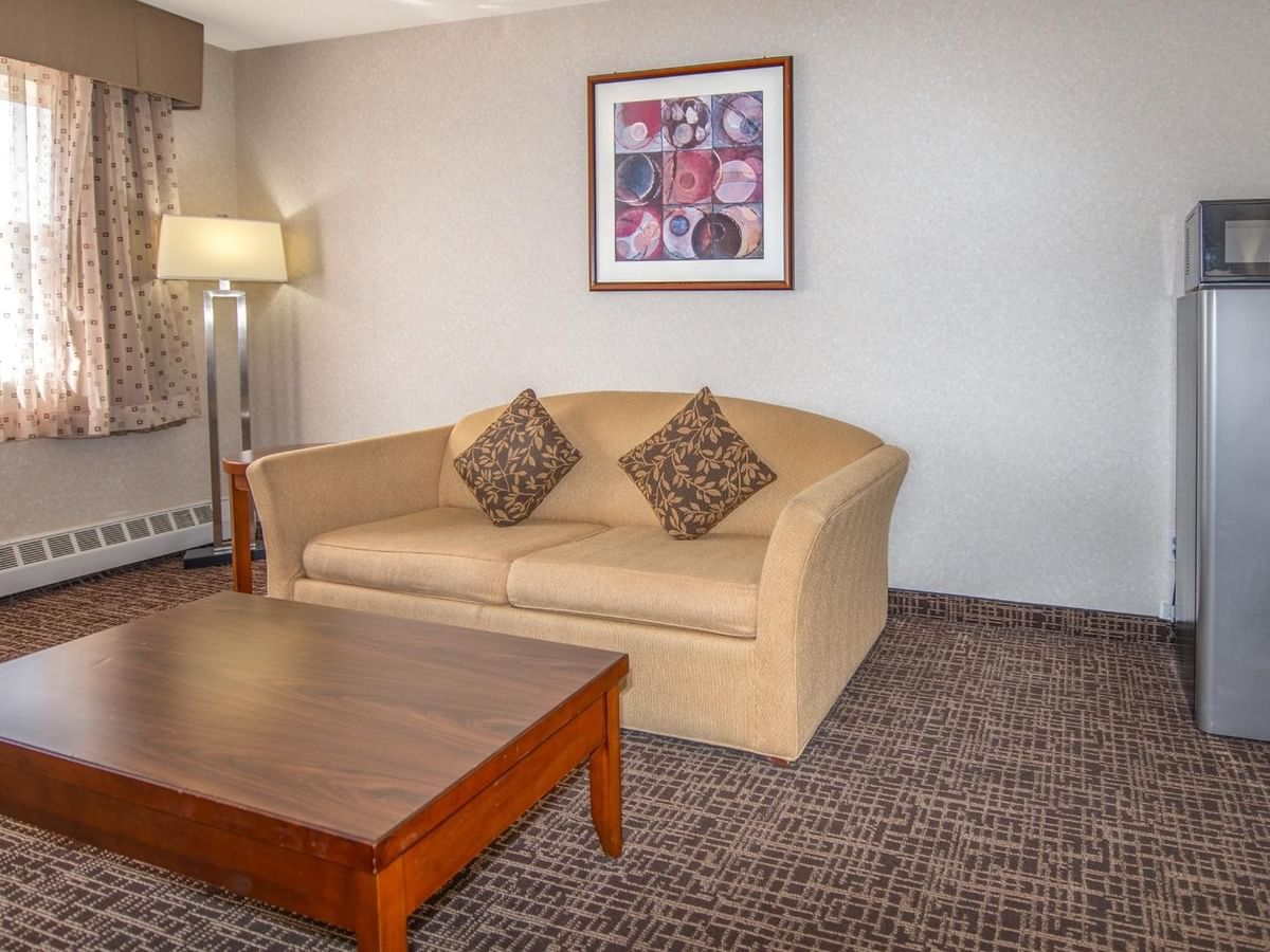 A hotel room with a couch, coffee table, lamp, refrigerator, microwave, and framed art.