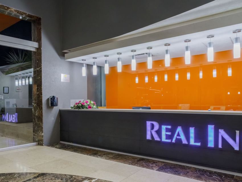 Night view of the reception showing the glowing logo and vibrant orange glass wall at Real Inn Torreon