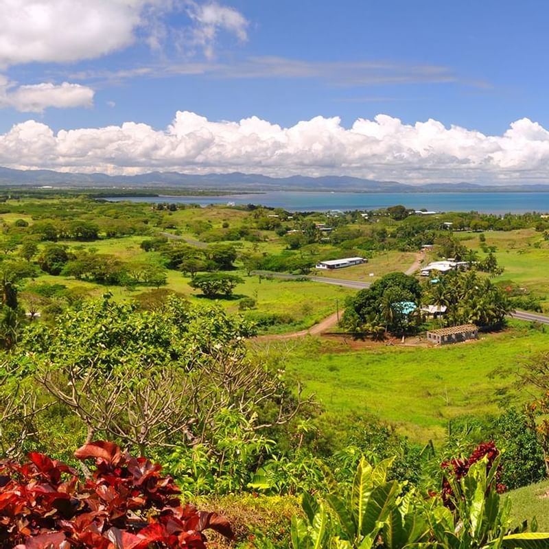 Vast green landscape with homes, a road, and a bay, featuring Nadi Fiji nature near Warwick Hotels and Resorts