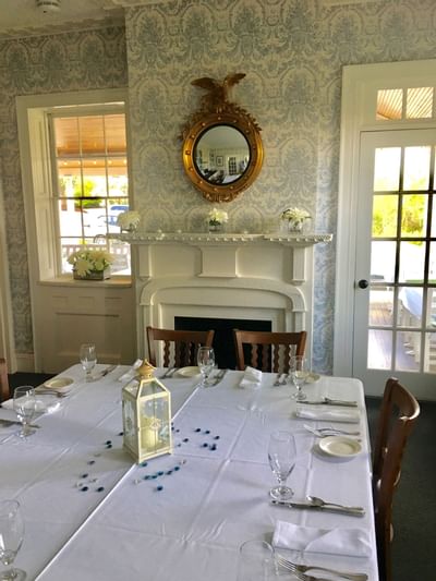 Long table set with glassware and a white lantern, under a gilded eagle mirror near French doors at Simsbury 1820 House