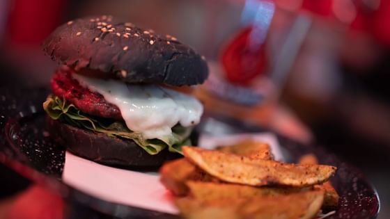 Gourmet burger on a black bun with melted cheese served with potato wedges at Media Sangre in Araiza Calafia