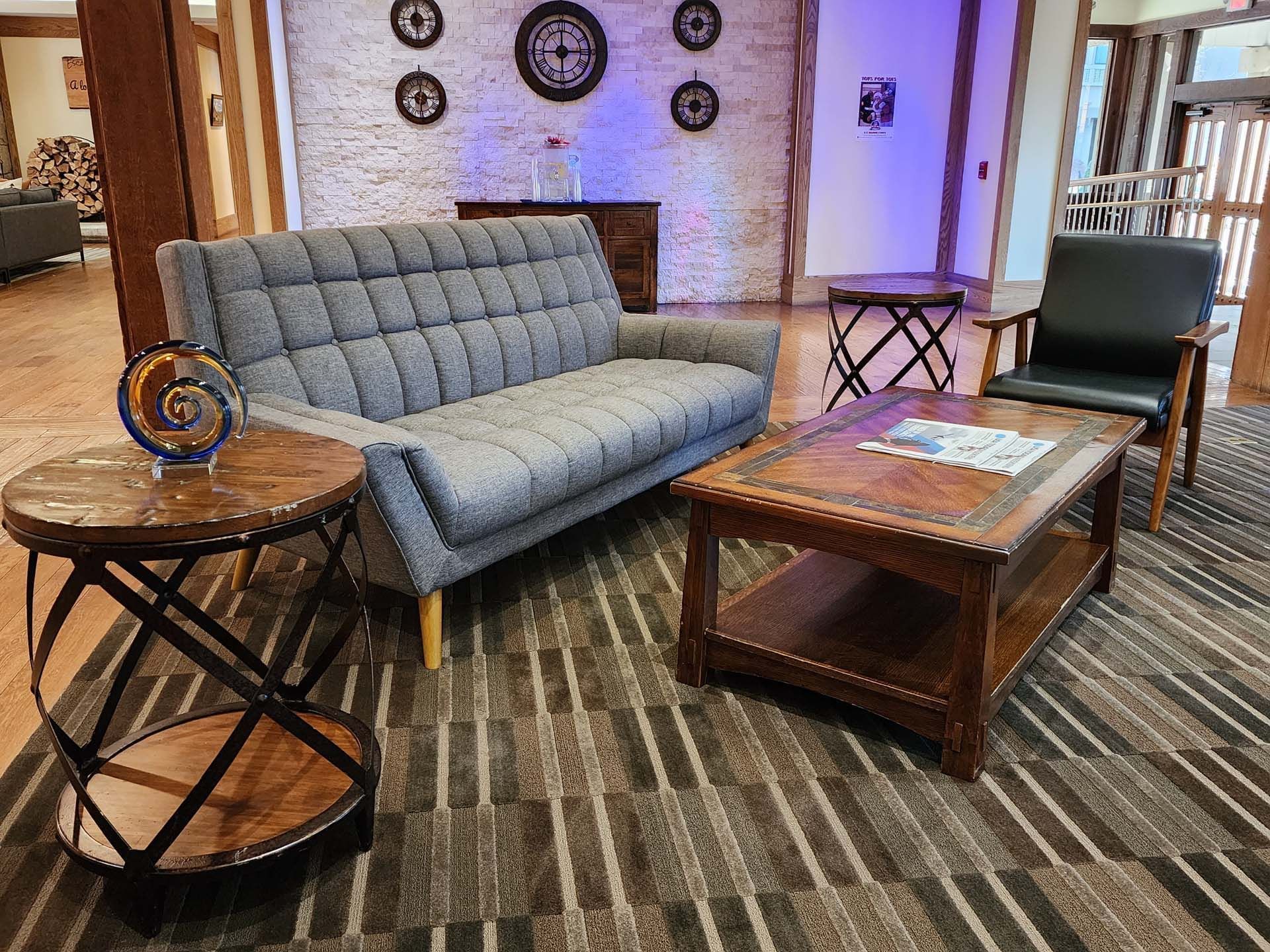 lobby with couch, chairs, end tables, clocks on the wall in back