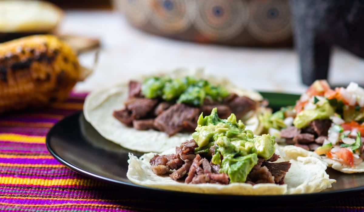 Tacos de res con guacamole y salsa sobre plato negro en Camino Real Hotels