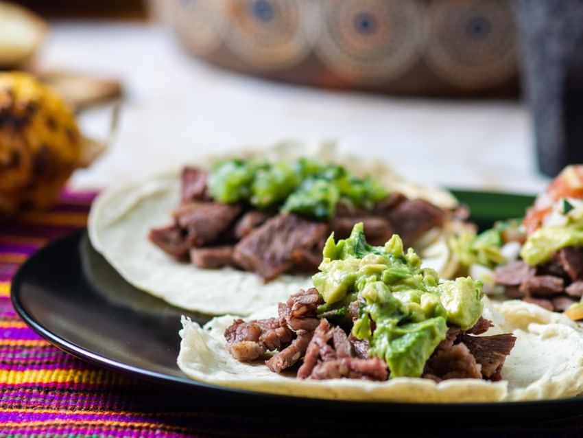 Tacos de carne con guacamole servidos en un plato negro cerca de Camino Real Hotels
