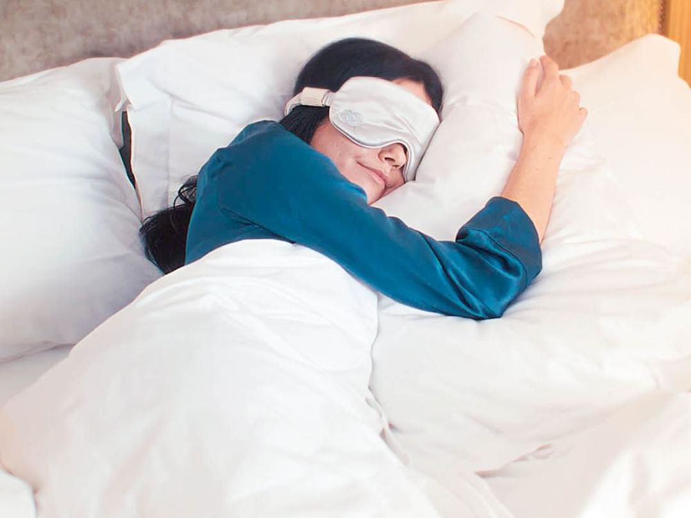 A woman peacefully sleeping in bed, wearing a white eye mask at Sofitel Brisbane Central