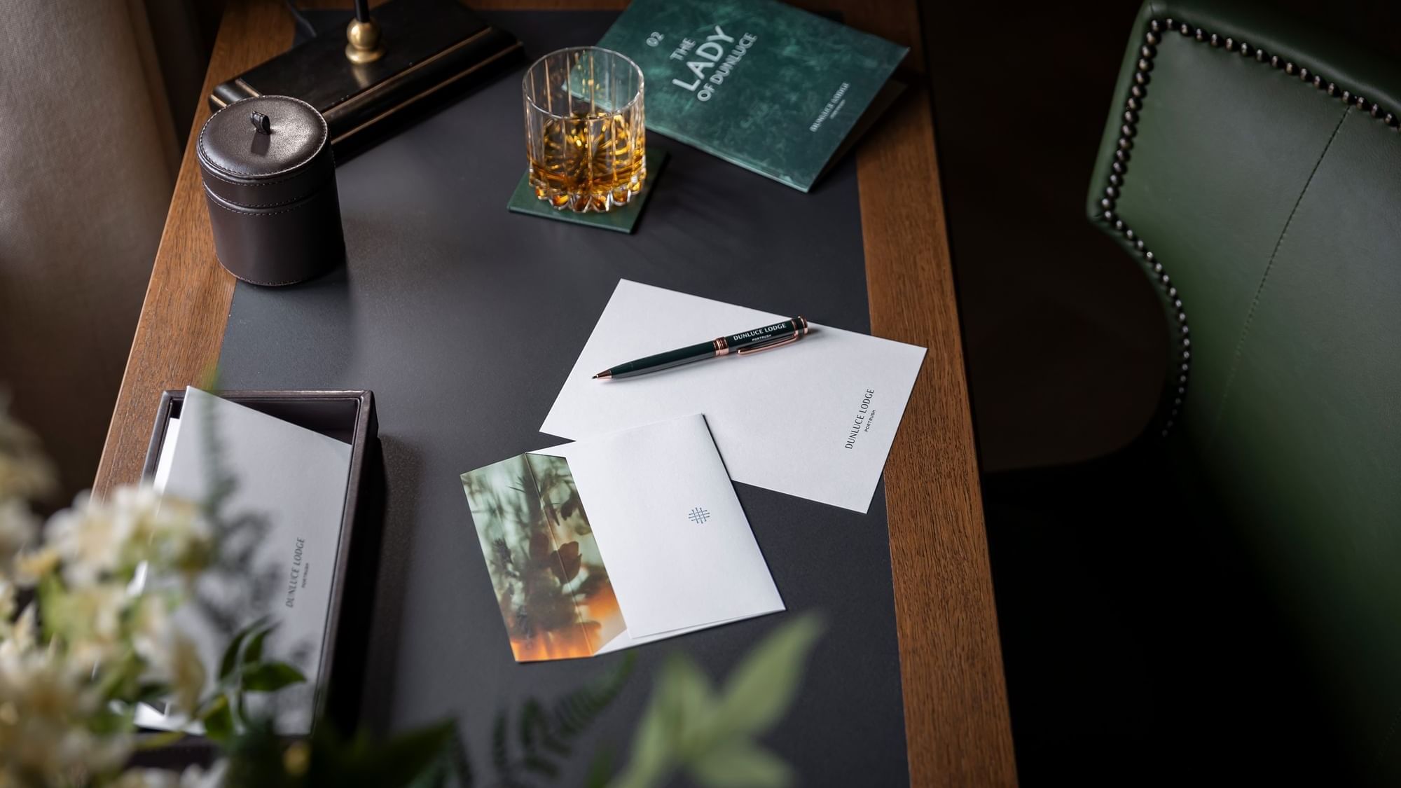 Writing desk with Dunluce Lodge stationery, a glass of whiskey, and a green notebook in Causeway Suite at Dunluce Lodge