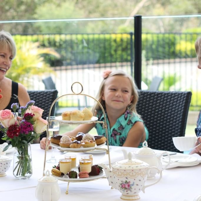 Three smiling women at a table with tea and pastries at Mercure Charlestown.