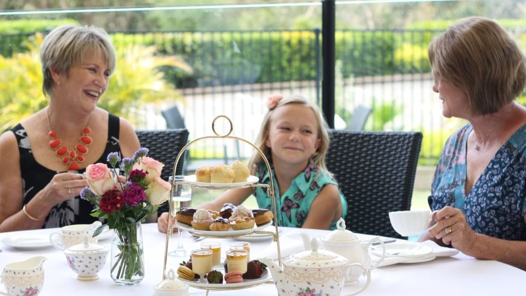 Three smiling women at a table with tea and pastries at Mercure Charlestown.