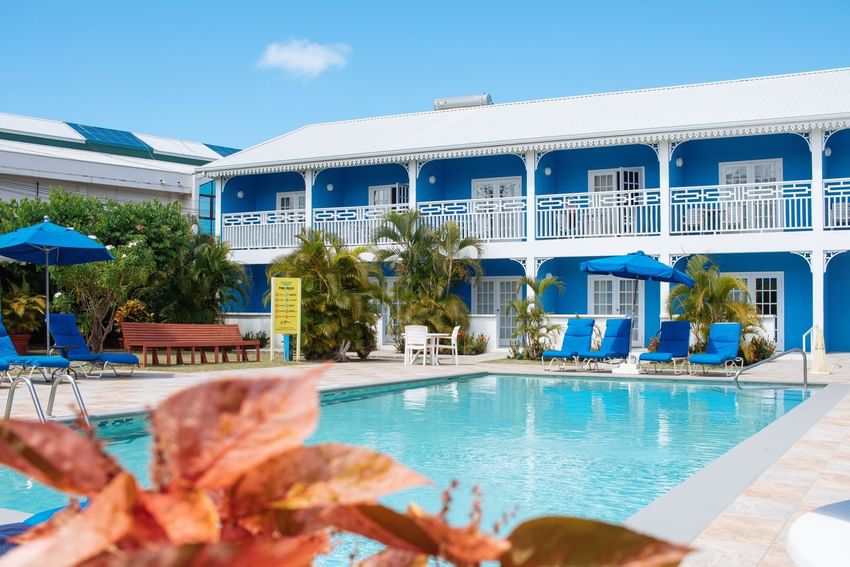 Bay Gardens Hotels and Resorts’ pool area with lounge chairs, umbrellas, and lush greenery under a clear blue sky