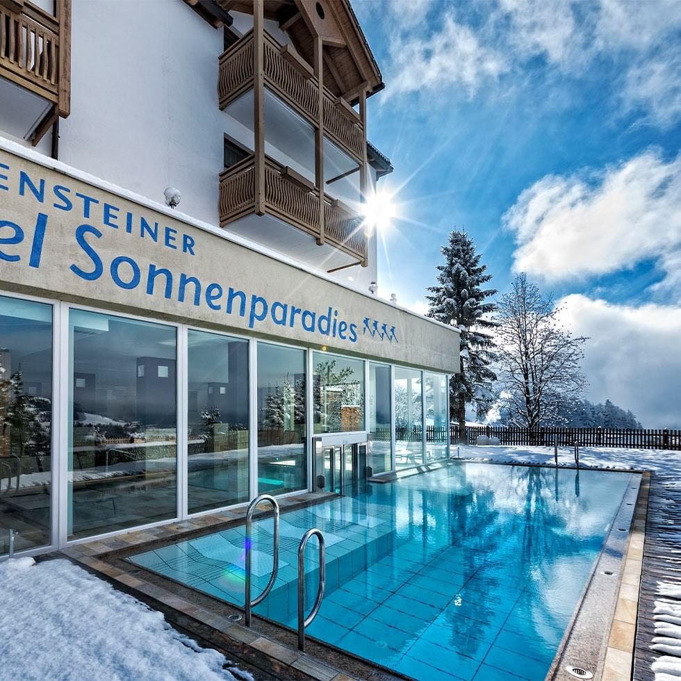 Outdoor pool with snow-covered ground in front of Hotel Sonnenparadies building.