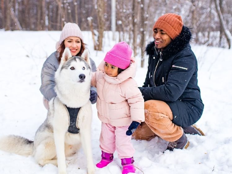 Family and dog smiling in snowy landscape.
