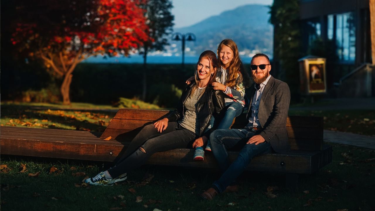 Family of three smiling on a park bench with scenic mountain view in background.