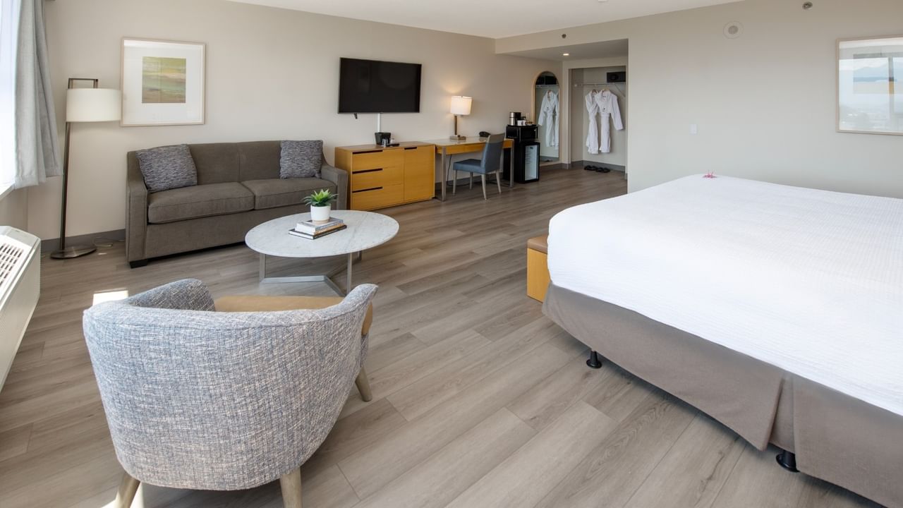 A hotel room with a large king bed, couch, chair, work desk, and TV.