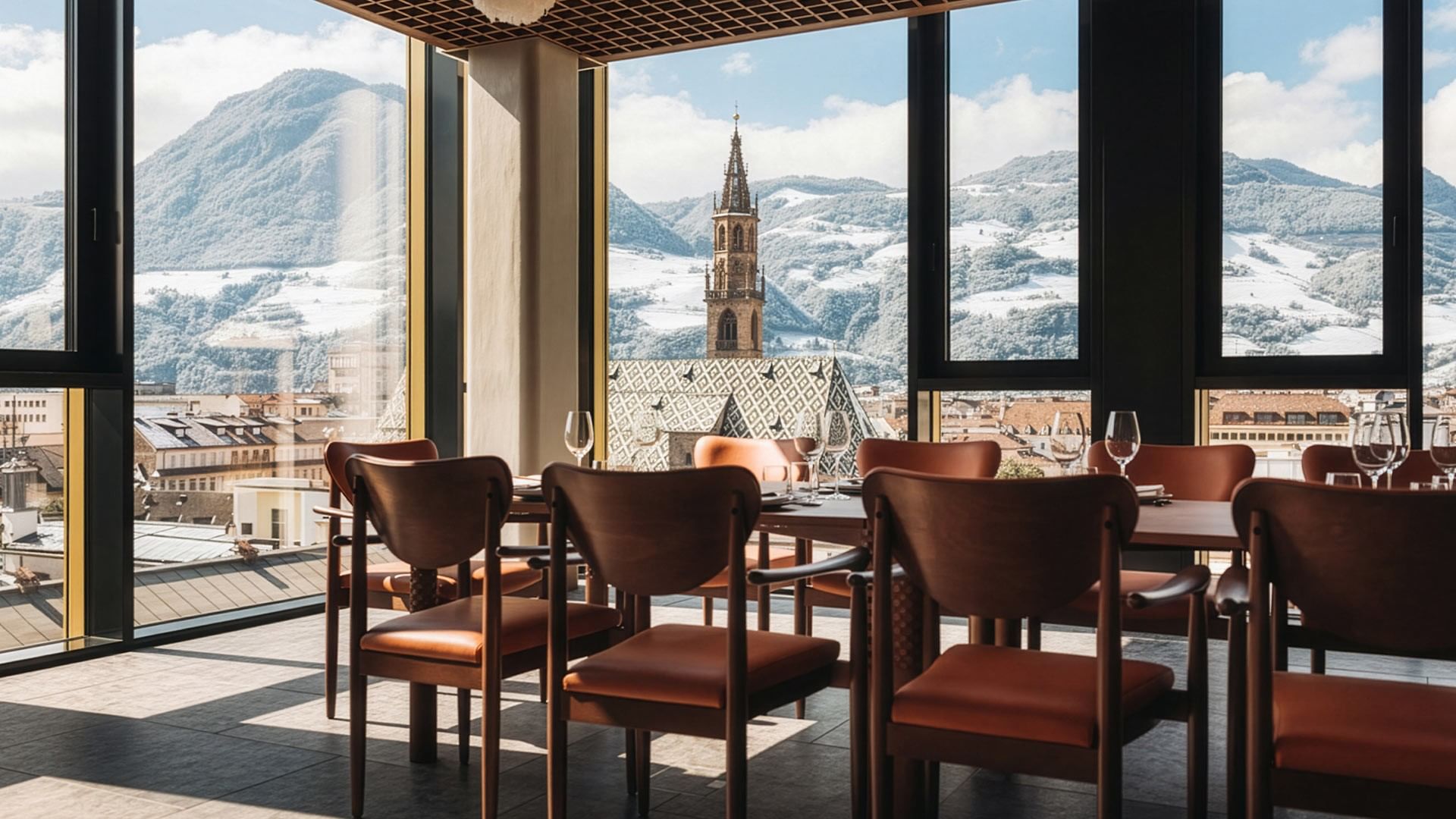 Esstisch mit Stühlen und Panoramablick auf eine Stadt und verschneite Berge durch große Fenster.