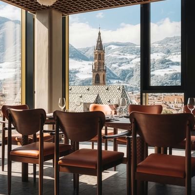 Speisesaal mit Panoramablick auf verschneite Berge und eine Kirche durch große Fenster.