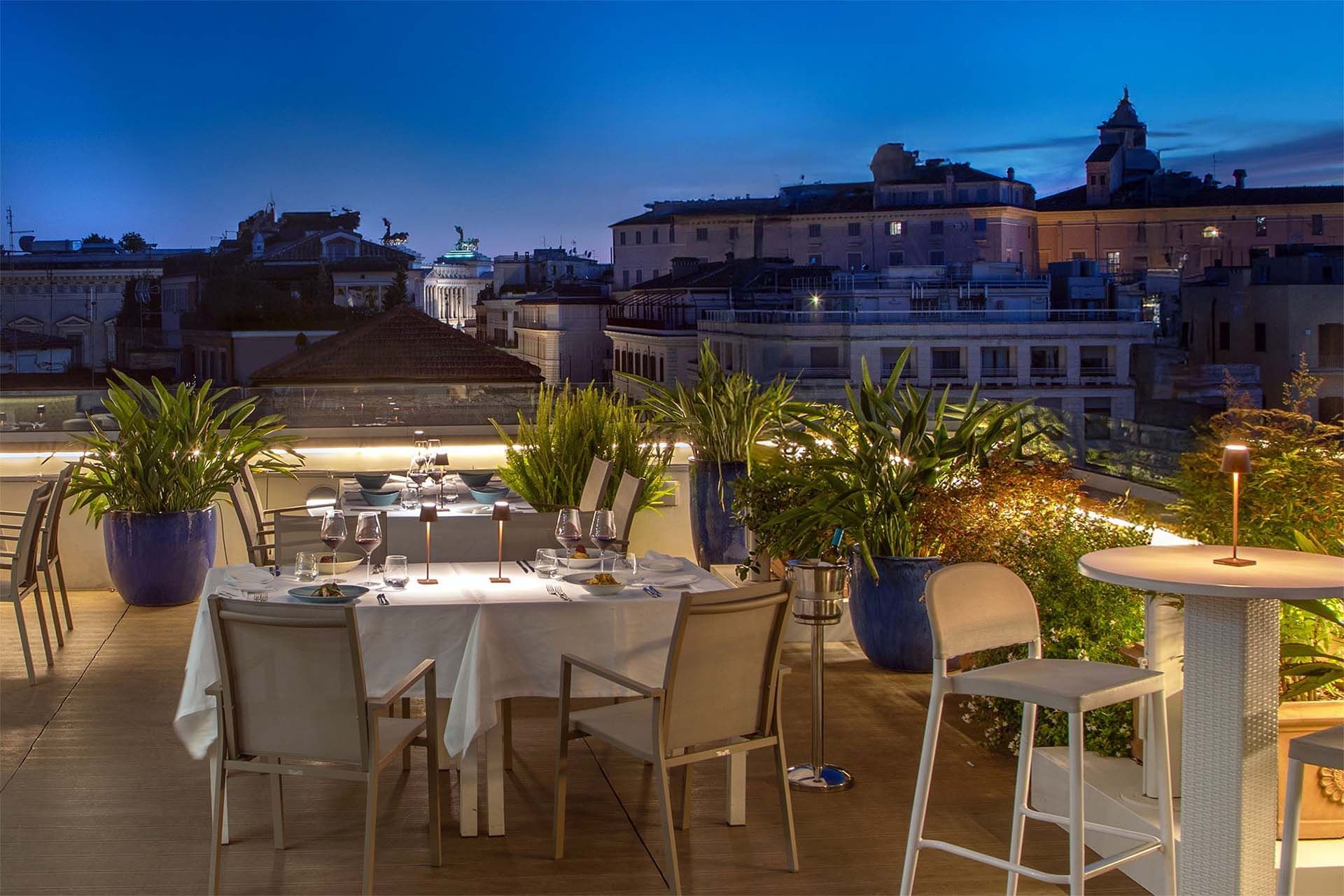 Terrazza Monti rooftop dining area with a set table, surrounded by greenery and city views at The Glam Hotel