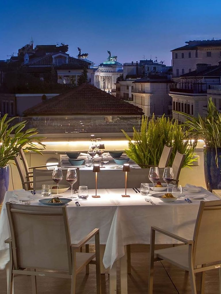 Terrazza Monti rooftop dining area with a set table, surrounded by greenery and city views at The Glam Hotel