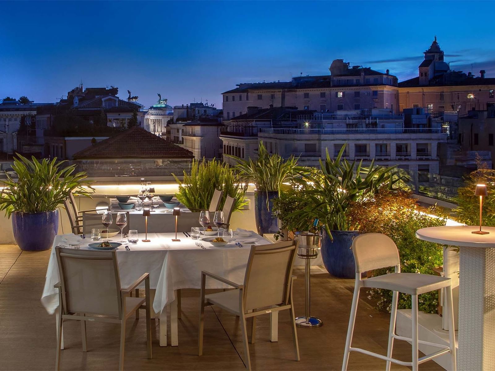 Terrazza Monti rooftop dining area with a set table, surrounded by greenery and city views at The Glam Hotel