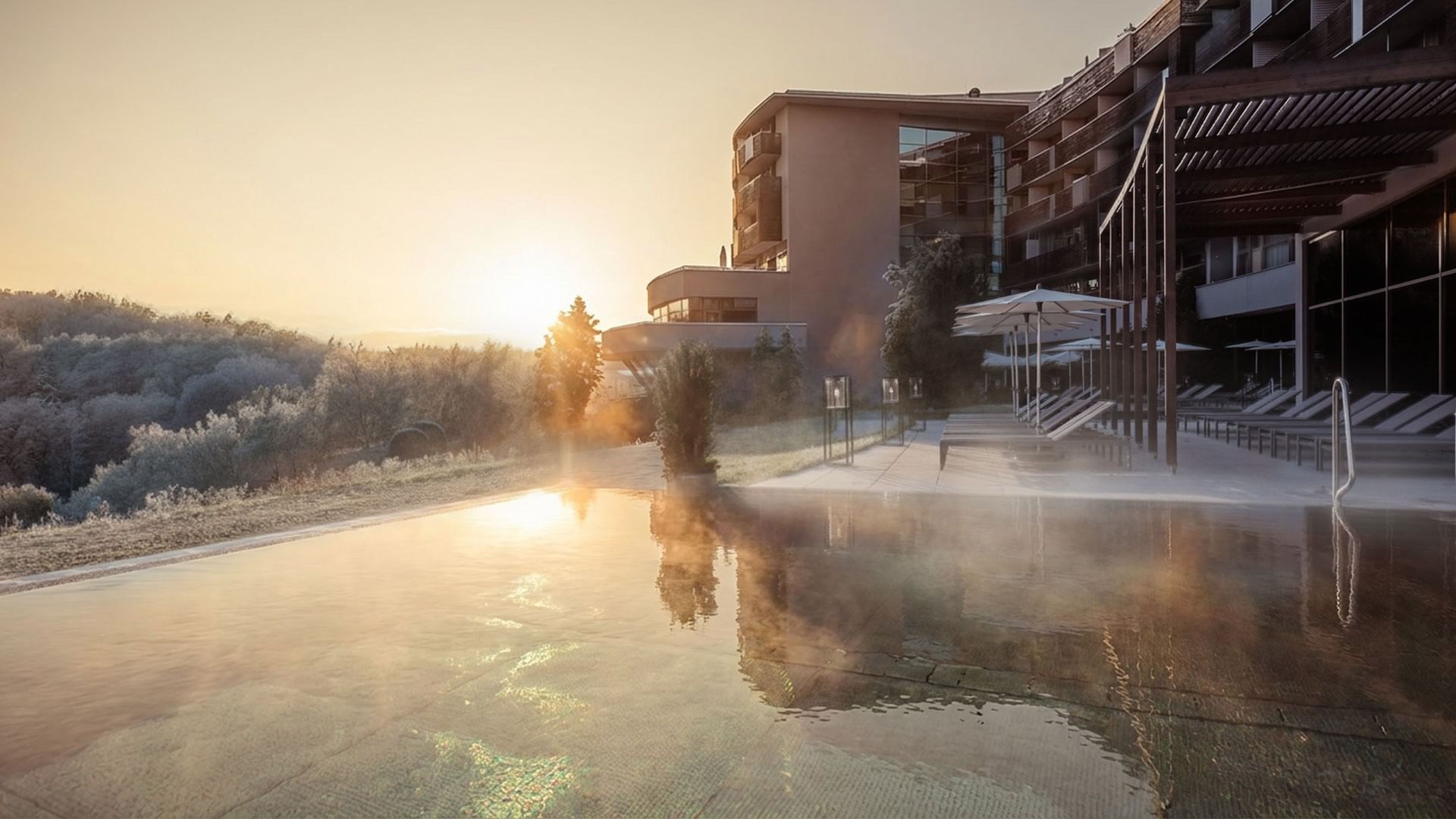 Sonnenaufgang über Hotelpool mit Loungebereich und Bäumen bei Falkensteiner Balance Resort Stegersbach
