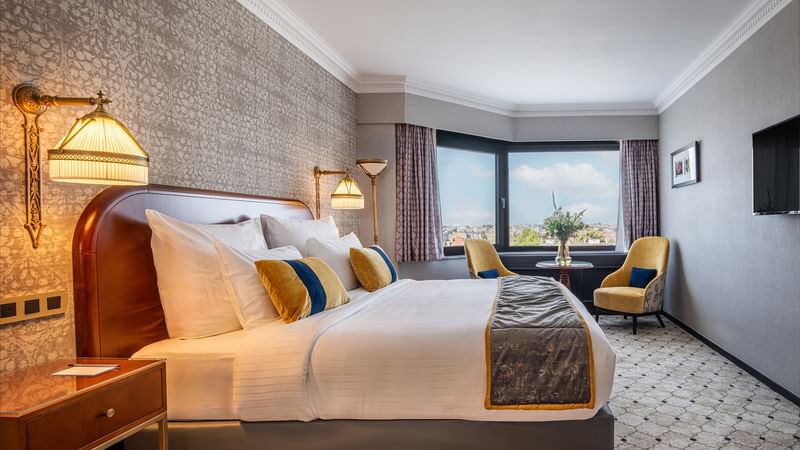 Deluxe  room at Hotel Barsey with a large bed, two chairs, a table, and a view of the city.