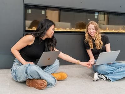 Two students sitting on the floor with laptops, studying together near the fireplace in the Laurent lobby.