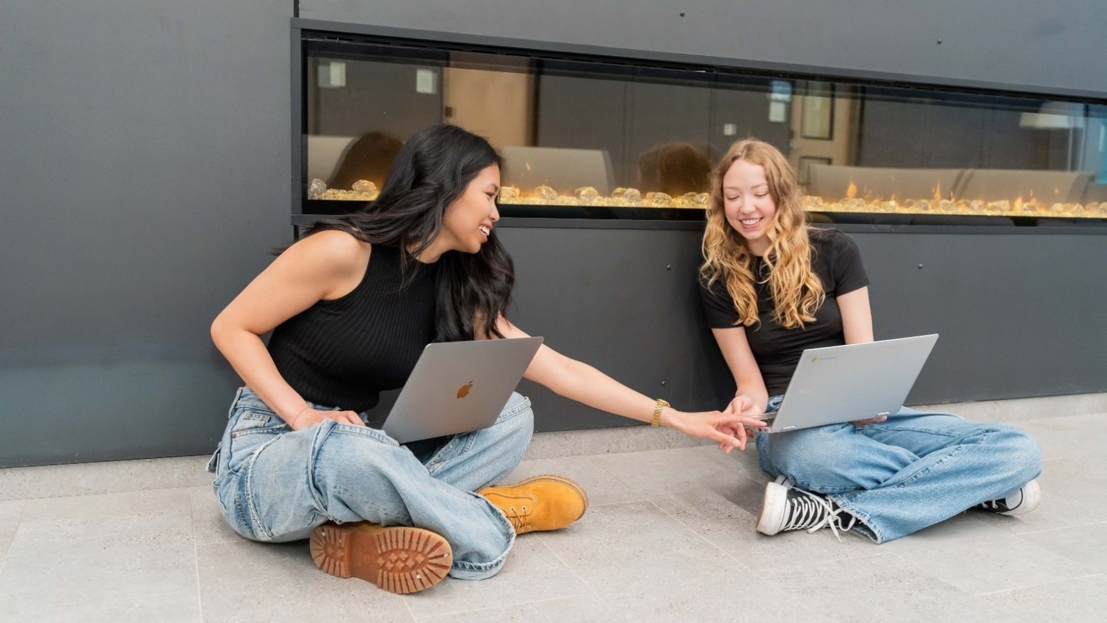 Two students sitting on the floor with laptops, studying together near the fireplace in the Laurent lobby.