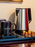 Black coffee mugs by a silver kettle and espresso machine in Family room with two queen beds at Warwick Paris Champs Elysées