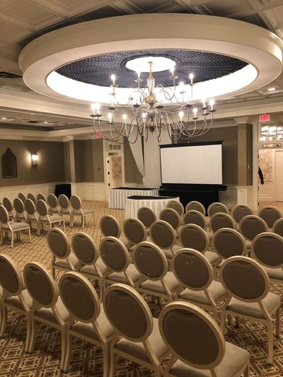 Rows of empty chairs facing a podium and screen under a grand chandelier in the Laurel Ballroom at The Simsbury Inn 