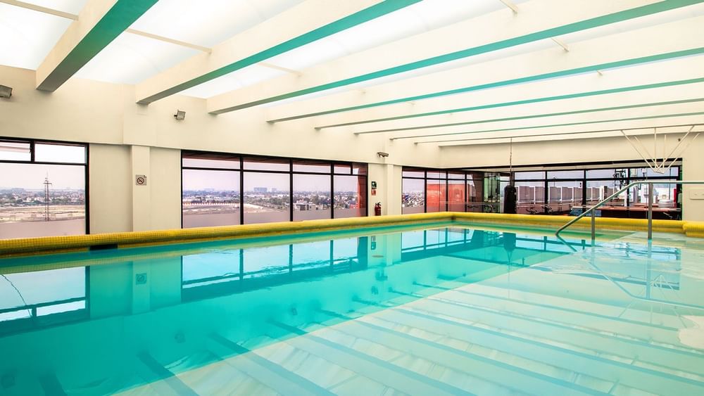 Indoor swimming pool with clear blue water and white ceiling beams at Camino Real Aeropuerto Mexico