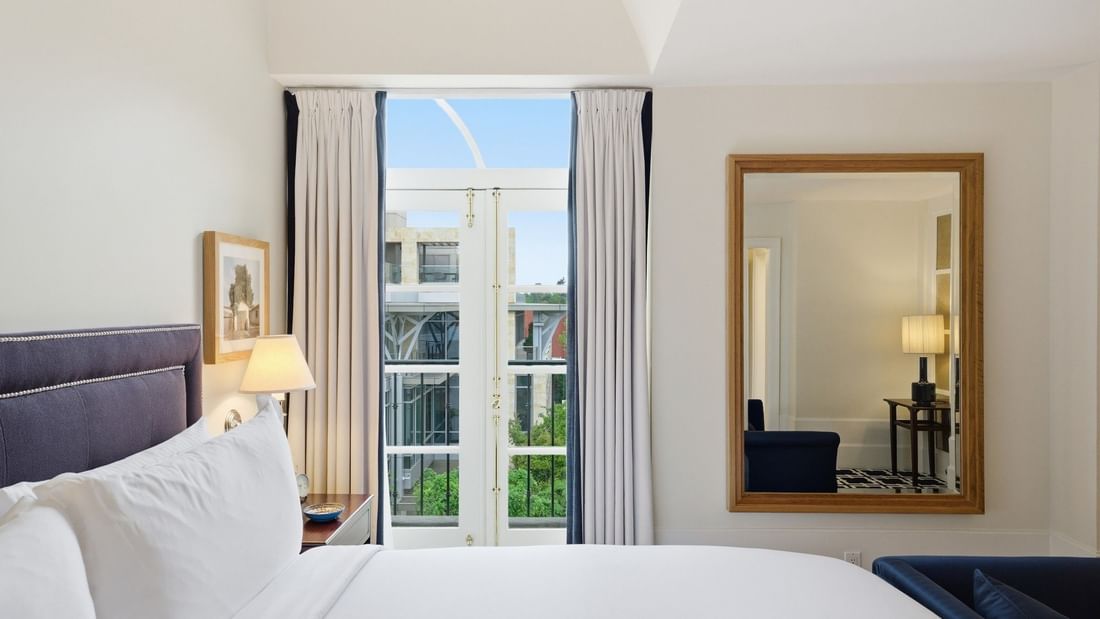 Grand Deluxe Suite with white bedding, tall windows, and mirror reflecting adjacent sitting area at el PRADO Hotel