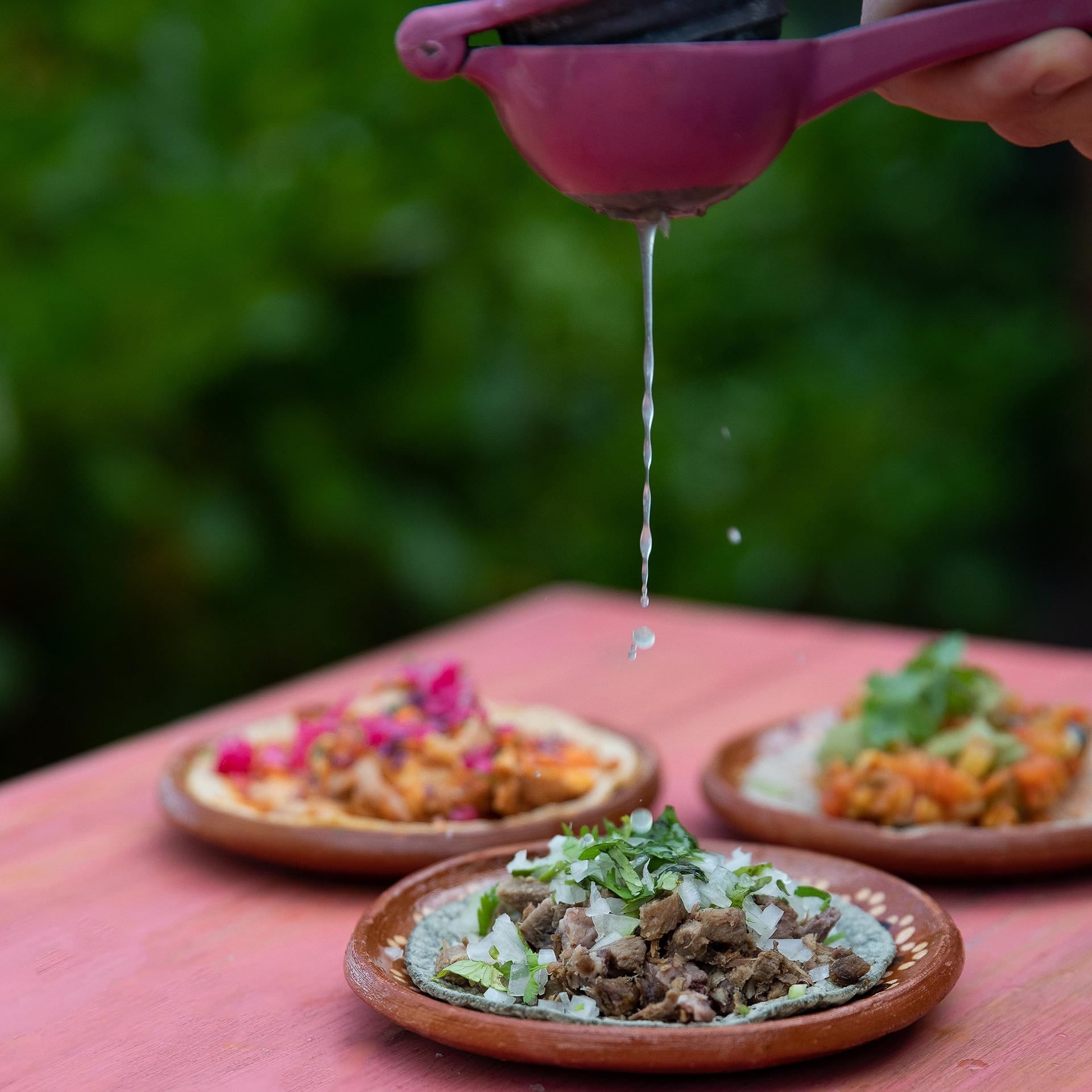 Fresh lime juice falling onto tacos served on terracotta plates at La Zebra.
