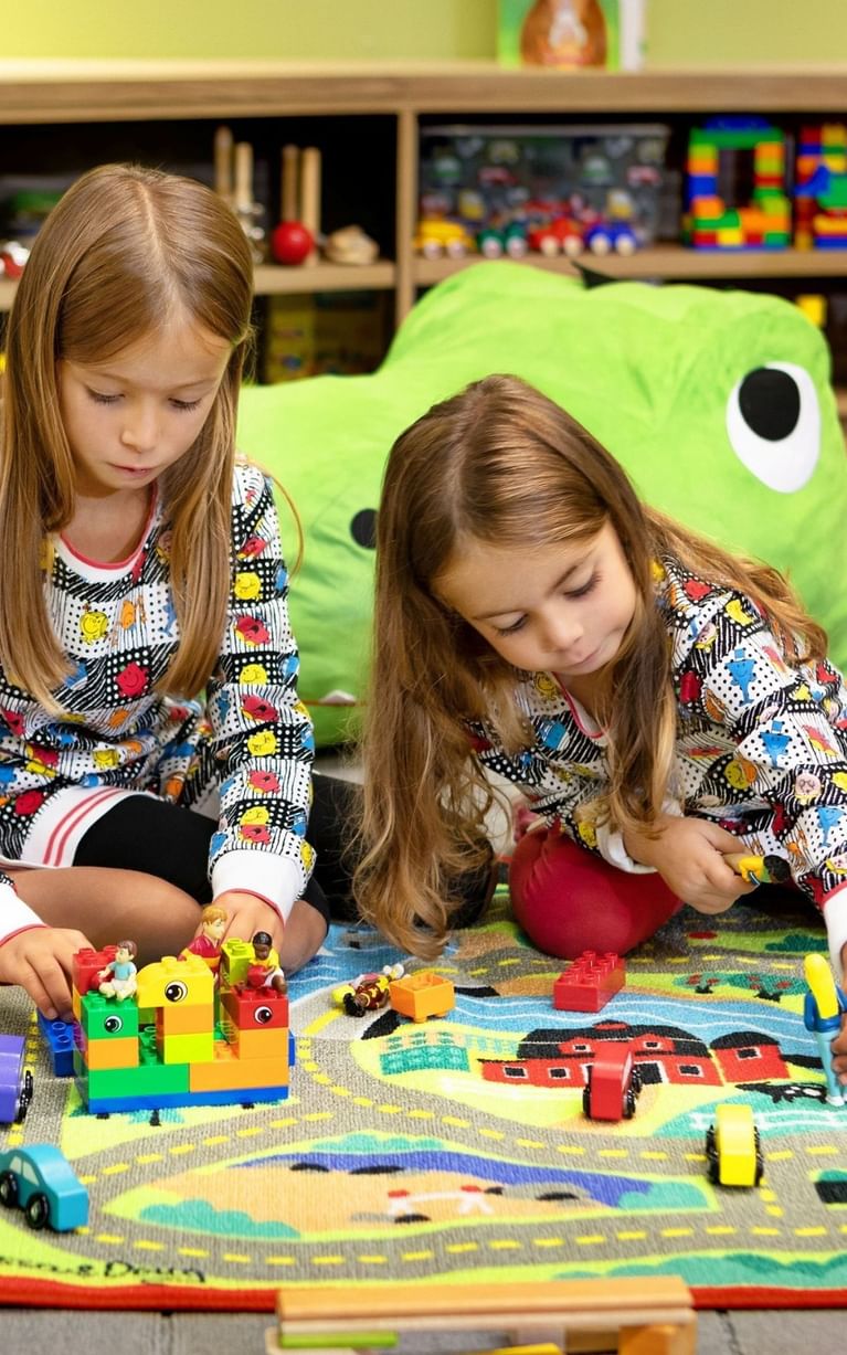 Two children playing with colorful building blocks and toy cars on a patterned rug in the kids area at Hotel X Toronto