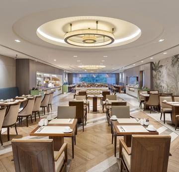 An elegant dining area with wooden tables and chairs, circular ceiling lights, and a tropical mural on the wall in Alesta Restaurant at Titanic Port Bakırköy