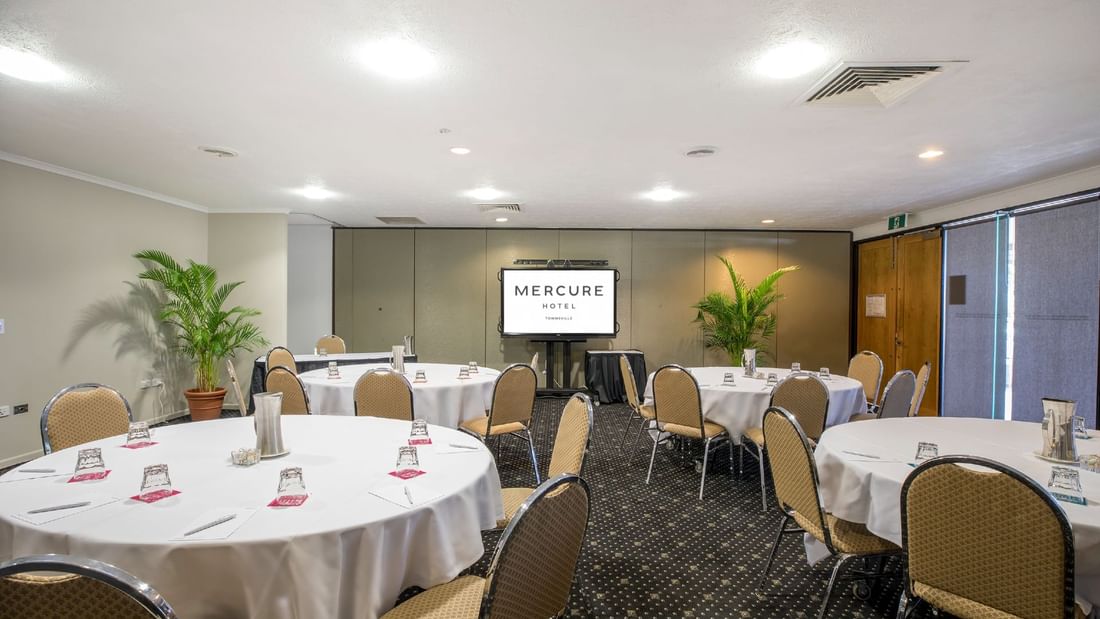 Tinaroo Room with cabaret table set, chairs and a projector screen at Mercure Hotel Townsville