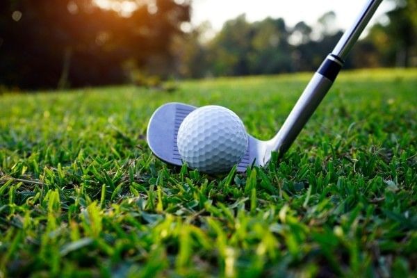 Close up of a golf ball beside a golf club on the grass.