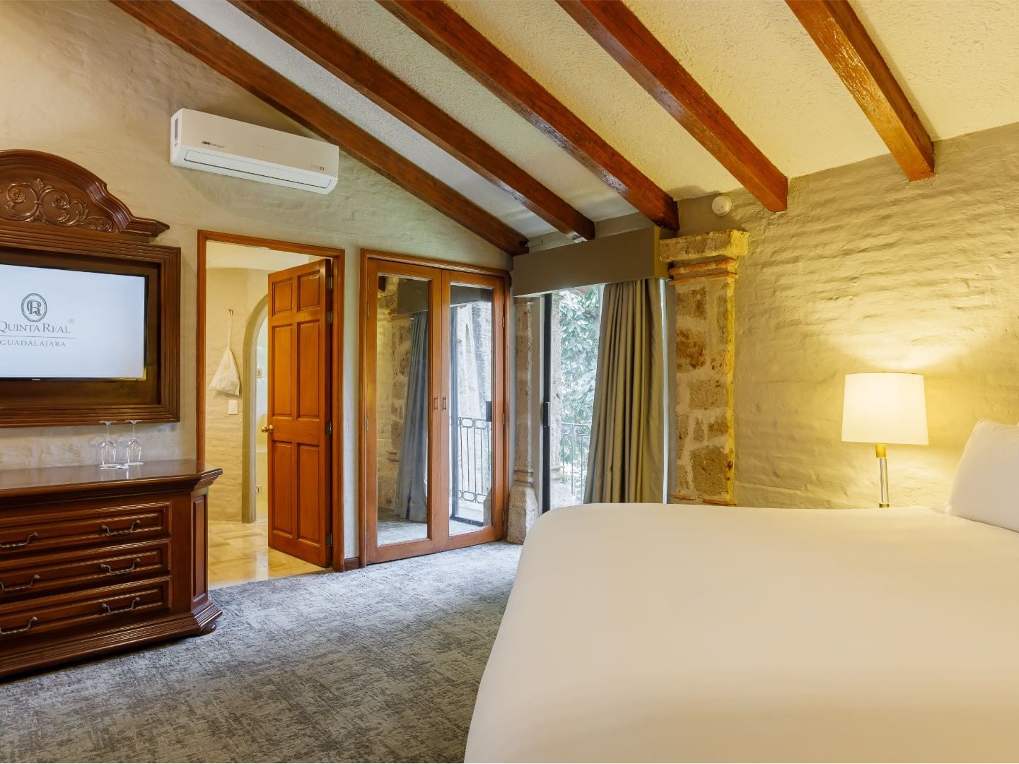 King Presidential Suite with a sloped wood ceiling and a stone pillar by the balcony, at the Quinta Real Guadalajara