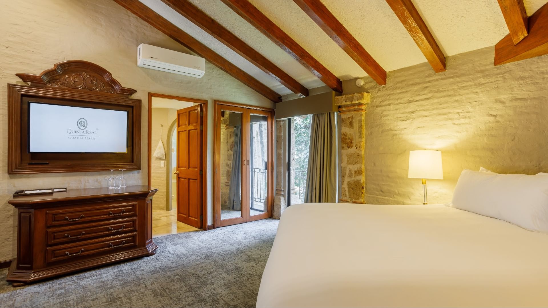 King Presidential Suite with a sloped wood ceiling and a stone pillar by the balcony, at the Quinta Real Guadalajara