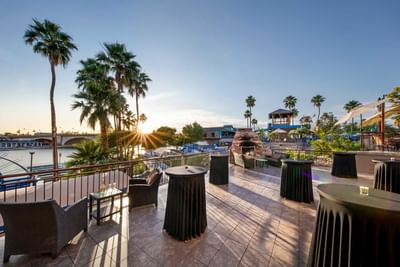Waterfront patio with cocktail tables, palm trees, and sunset views over the bridge at London Bridge Resort