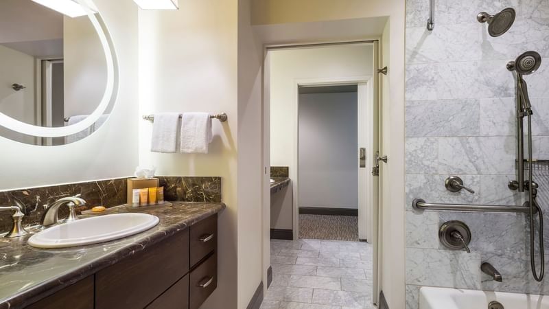 White sink on a dark wood vanity by a marble shower wall in Accessible Bathroom at Warwick Hotels & Resorts