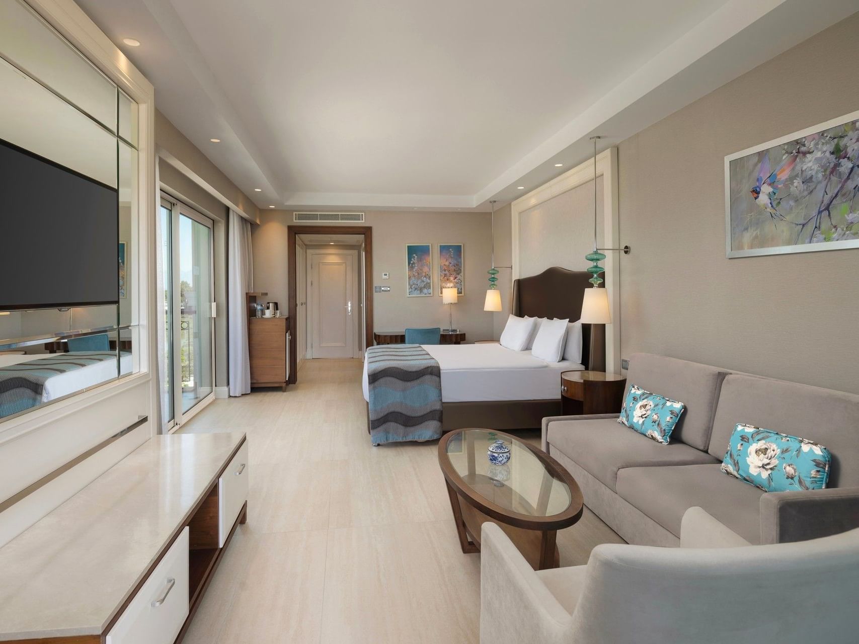 Spacious hotel suite with king bed, gray sofa, glass coffee table, balcony access, and modern amenities at Titanic Deluxe Golf Belek