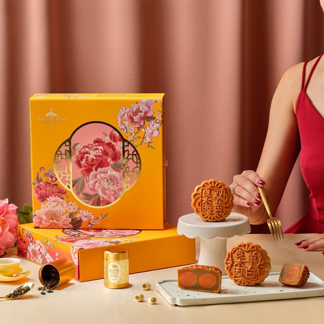 A woman in red posing with Goodwood Park Hotel mooncakes in a beautiful, yellow gift box and tea set