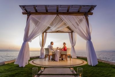 A couple enjoys a sunset dinner under a canopy by the sea at Villa Premiere Boutique Hotel & Romantic Getaway