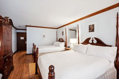 Two four-poster beds beside a small nightstand near a tall wooden armoire in the guest room at Avon Old Farms Hotel