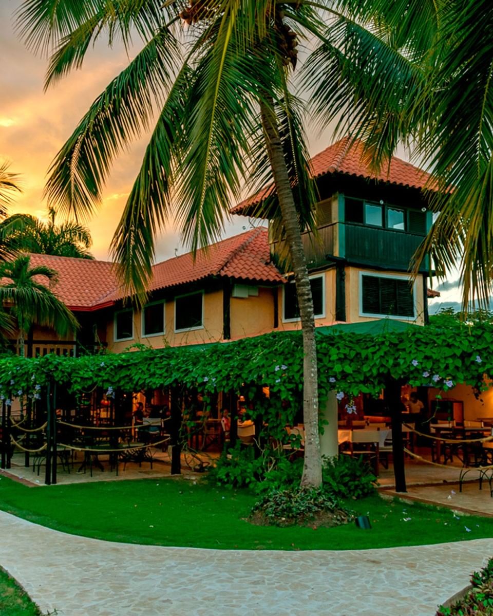 Garden Restaurant with a red-tiled roof surrounded by lush palm trees and greenery at Hotel La Casita by The Hub