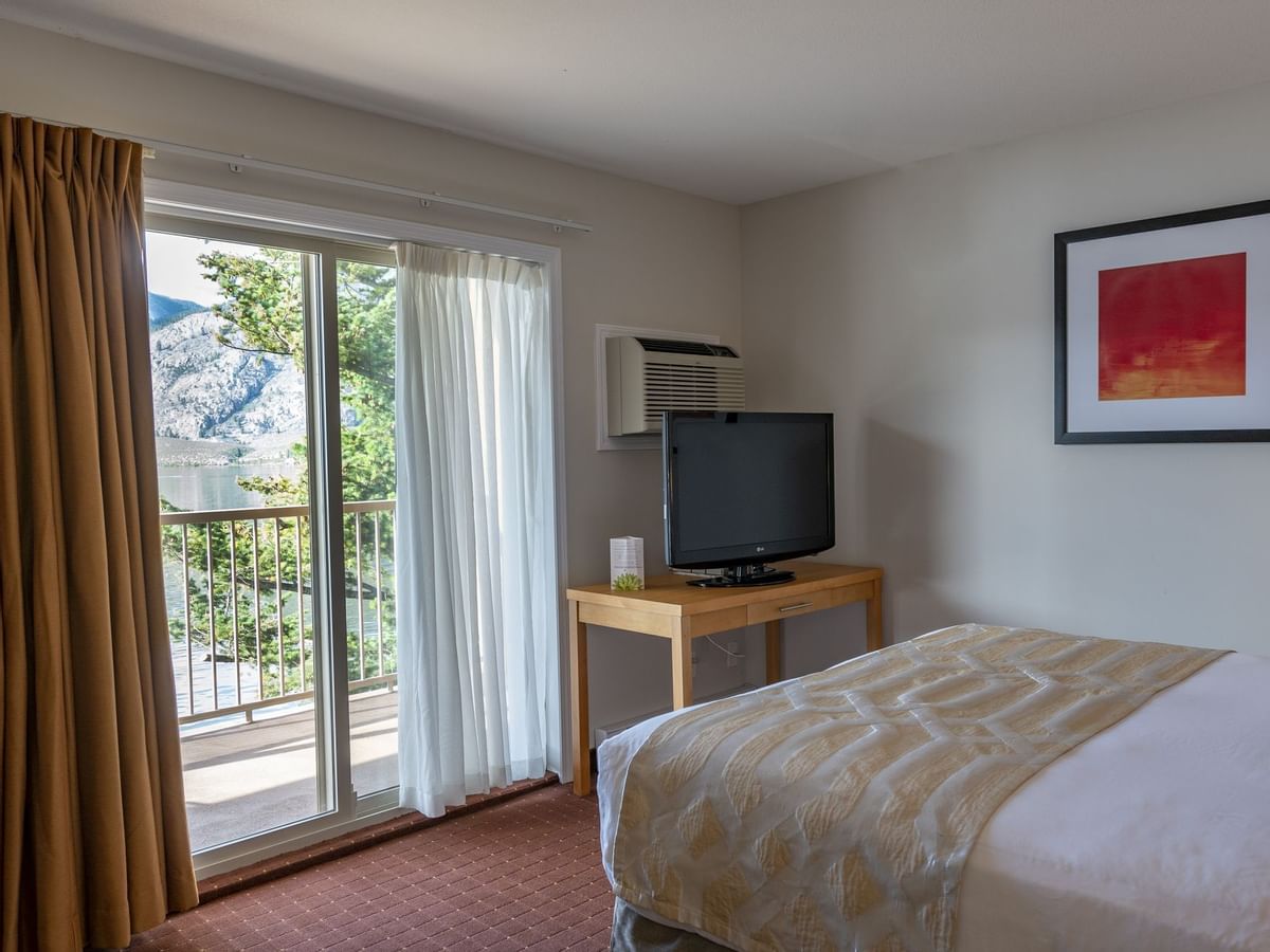 Bed and TV in hotel room with balcony and view of lake