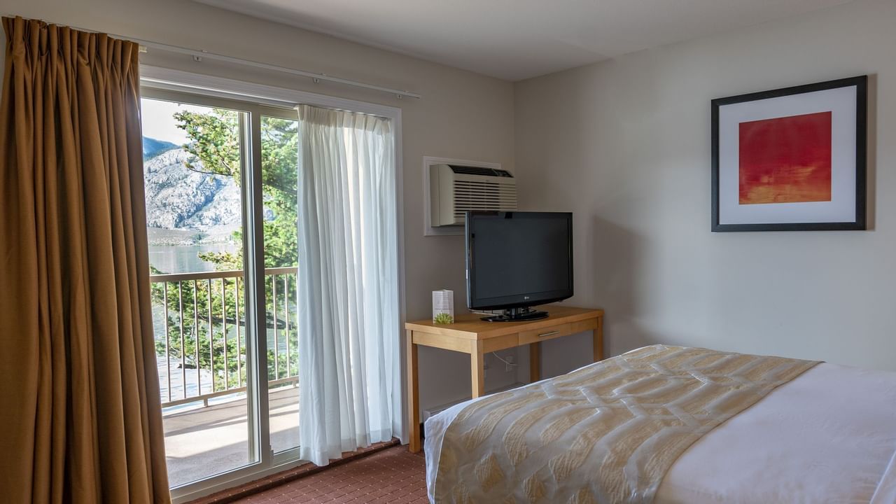 Bed and TV in hotel room with balcony and view of lake