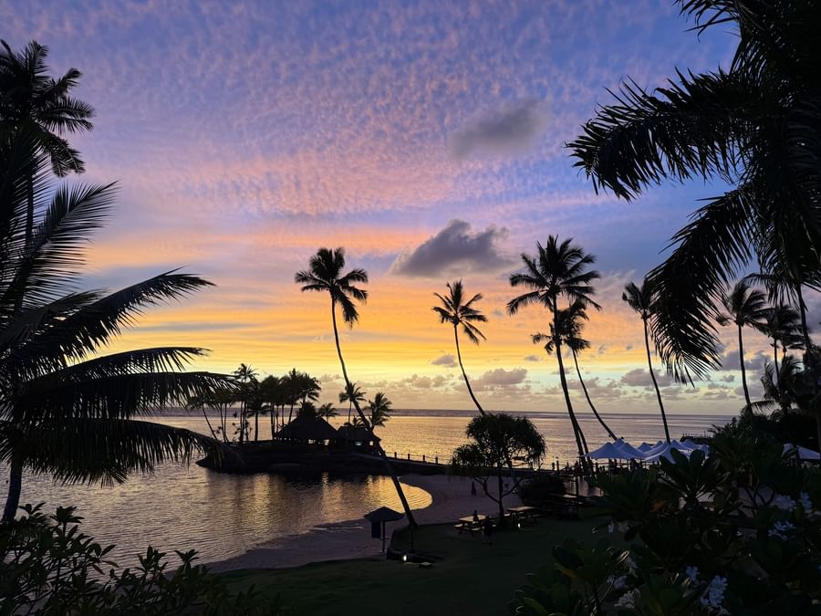 Sunset over ocean and beach view with palm trees at Warwick Fiji Resort and Spa.