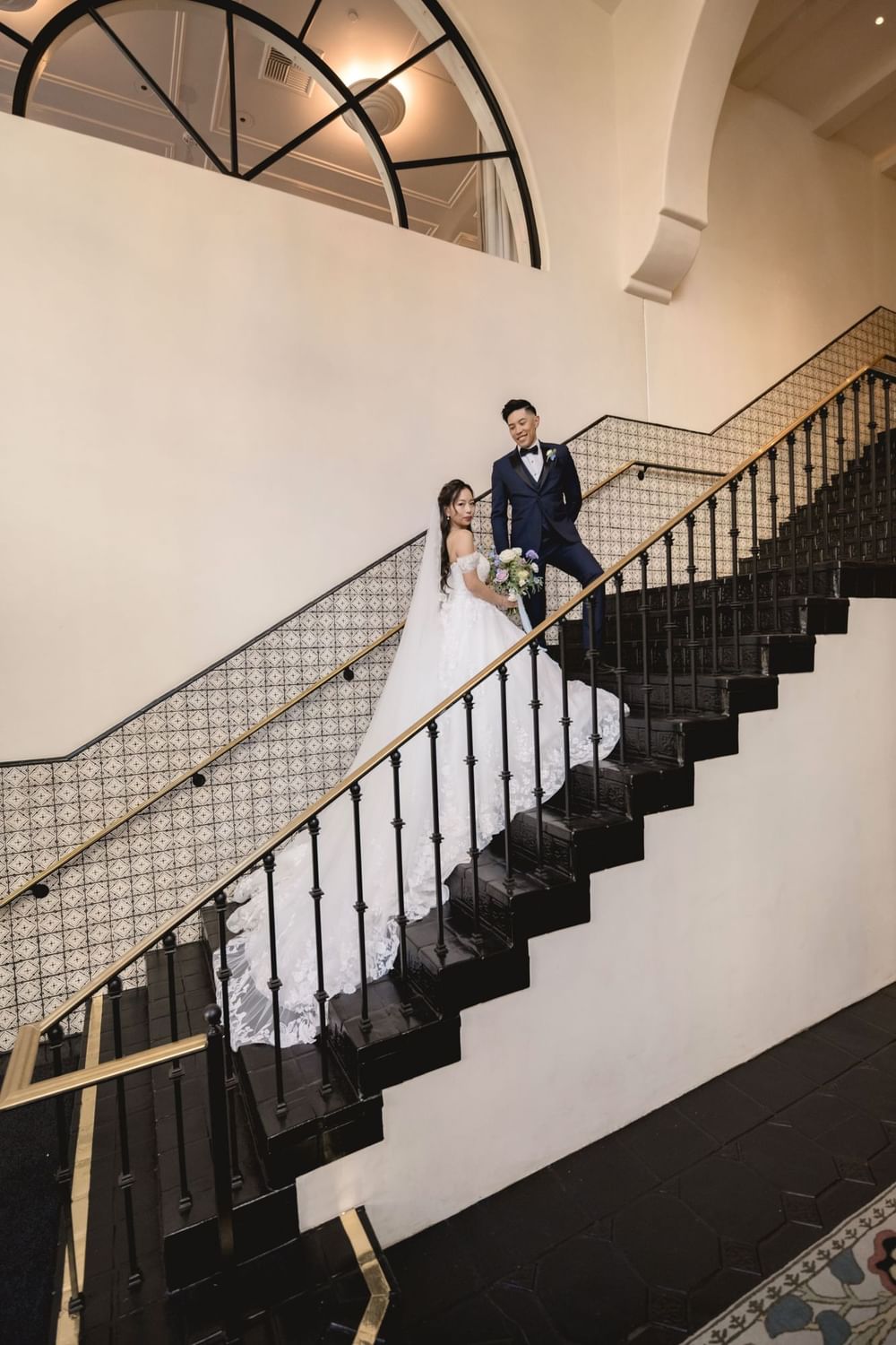 Bride and groom posing on the elegant grand staircase at El Prado Hotel