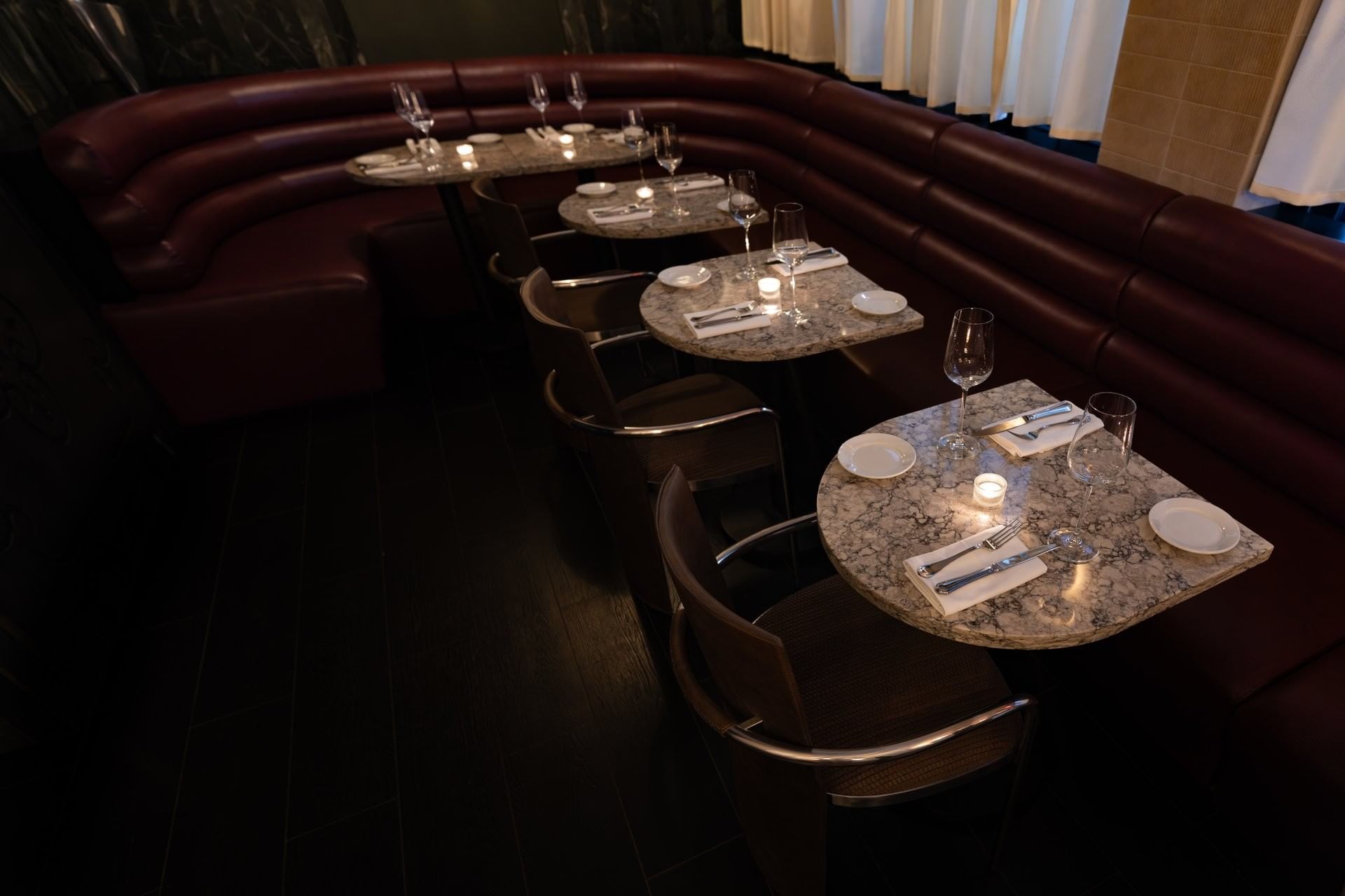 A dimly lit dining area with marble-topped tables and red leather booths.